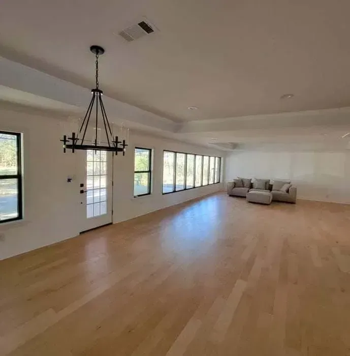 Spacious room with hardwood floors, windows, and a couch. A black chandelier hangs from the ceiling.