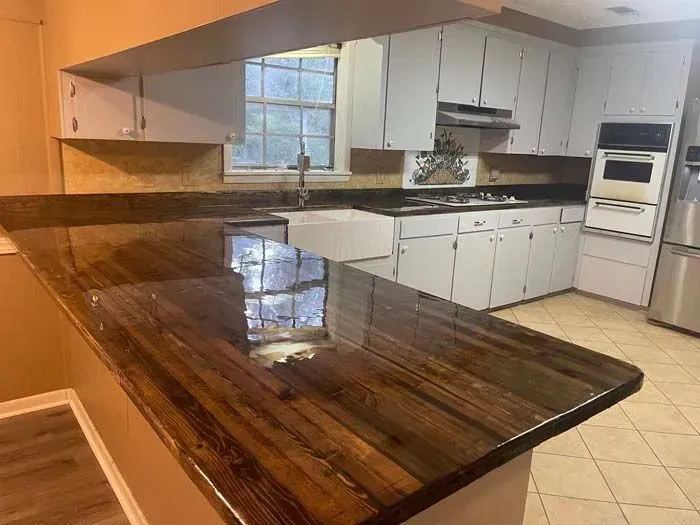 Brown countertop in a kitchen with white cabinets, window, and stainless steel appliances.