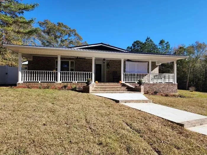Brick house with white porch and steps leading to the front door on a sunny day.