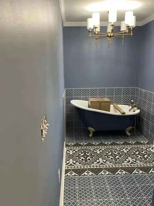 Blue bathroom with clawfoot tub, patterned tile floor, and modern chandelier.