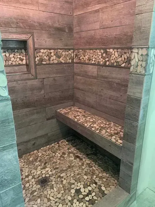 Shower with pebble floor, bench, and decorative pebble and wood-look tile.