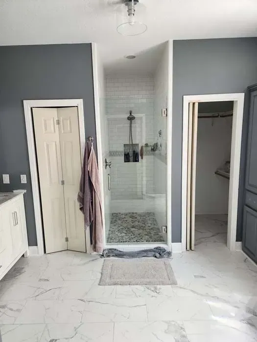 Bathroom with a shower, closet, and folding door; grey walls, white trim, and marble-look flooring.