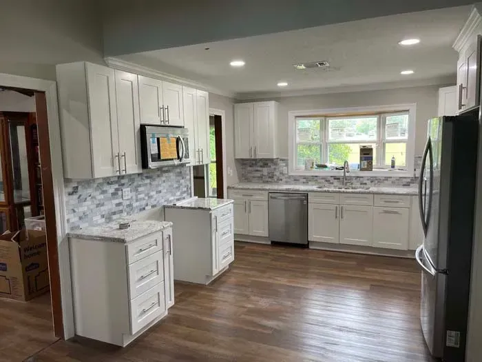 Newly renovated white kitchen with granite countertops, stainless steel appliances, and wood-look flooring.