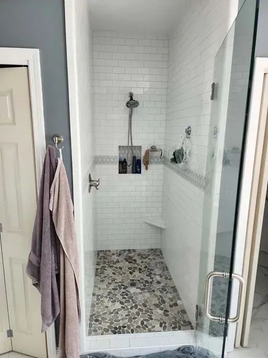 Narrow shower with white subway tiles, stone floor, glass door, and a built-in shelf.