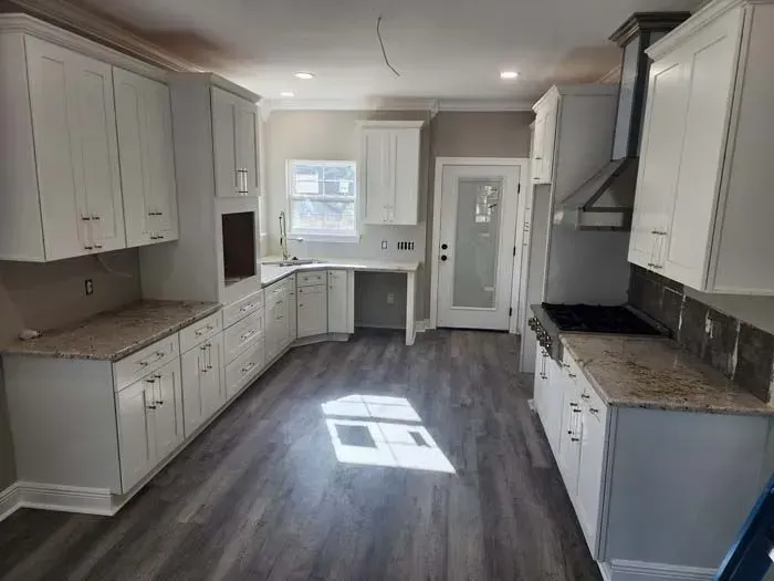 White kitchen with granite countertops, gray flooring, and a glass-paneled door.