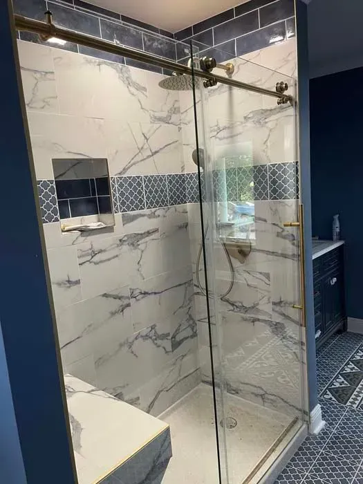 A newly renovated shower with marble-like white and blue tiles, glass door, and gold accents.