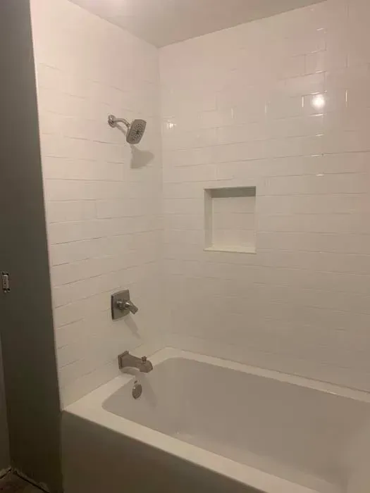 White tiled shower with built-in shelf, silver fixtures, and a bathtub.