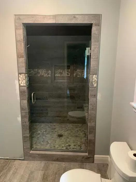 Shower with glass door and tiled frame, next to a toilet in a bathroom with neutral walls and flooring.
