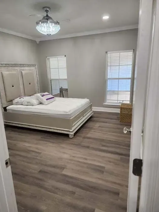 Bedroom with large bed, two windows, and wooden floor. Neutral colors, bright room.