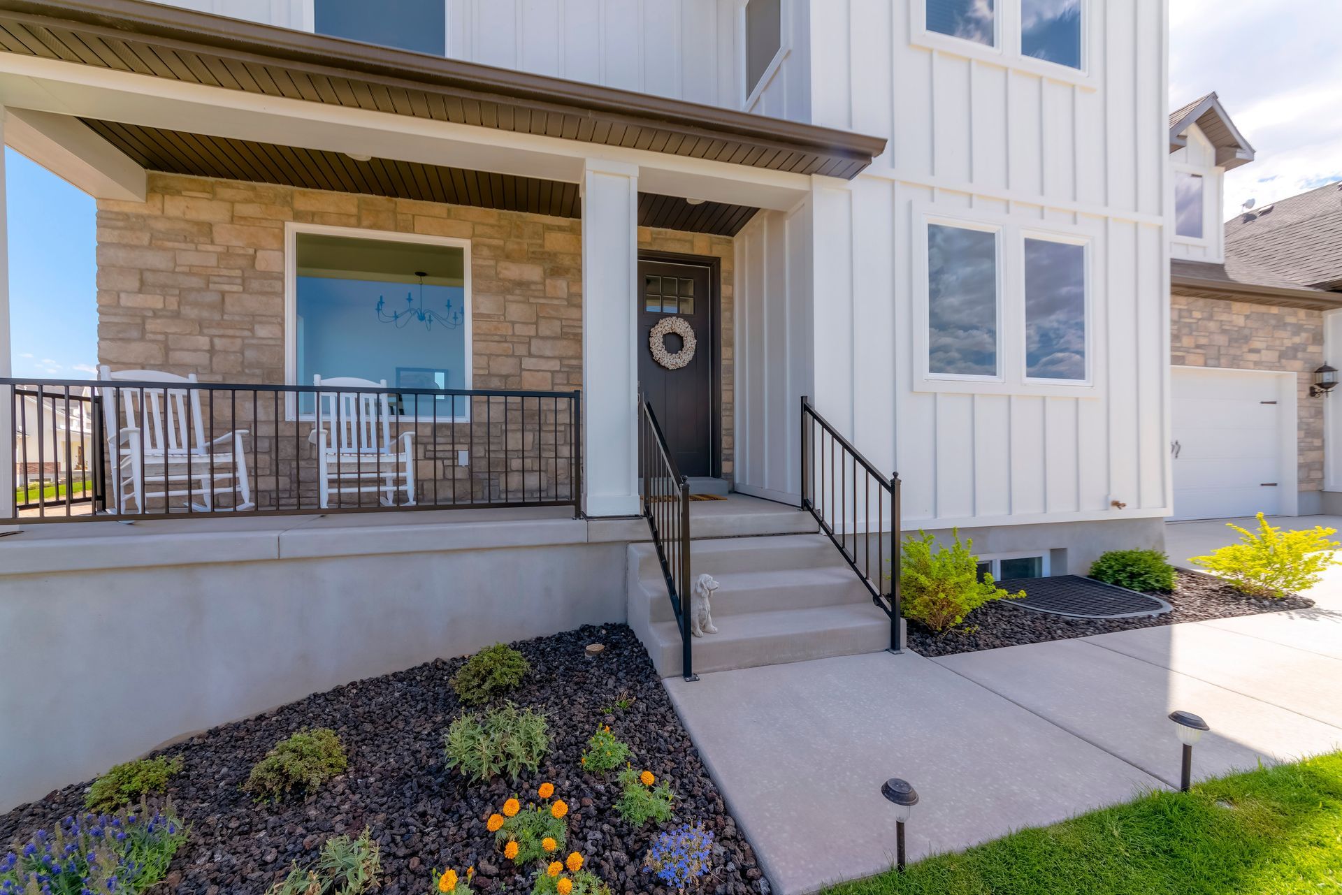 White two-story house with a porch, stone accents, and a small garden bed.