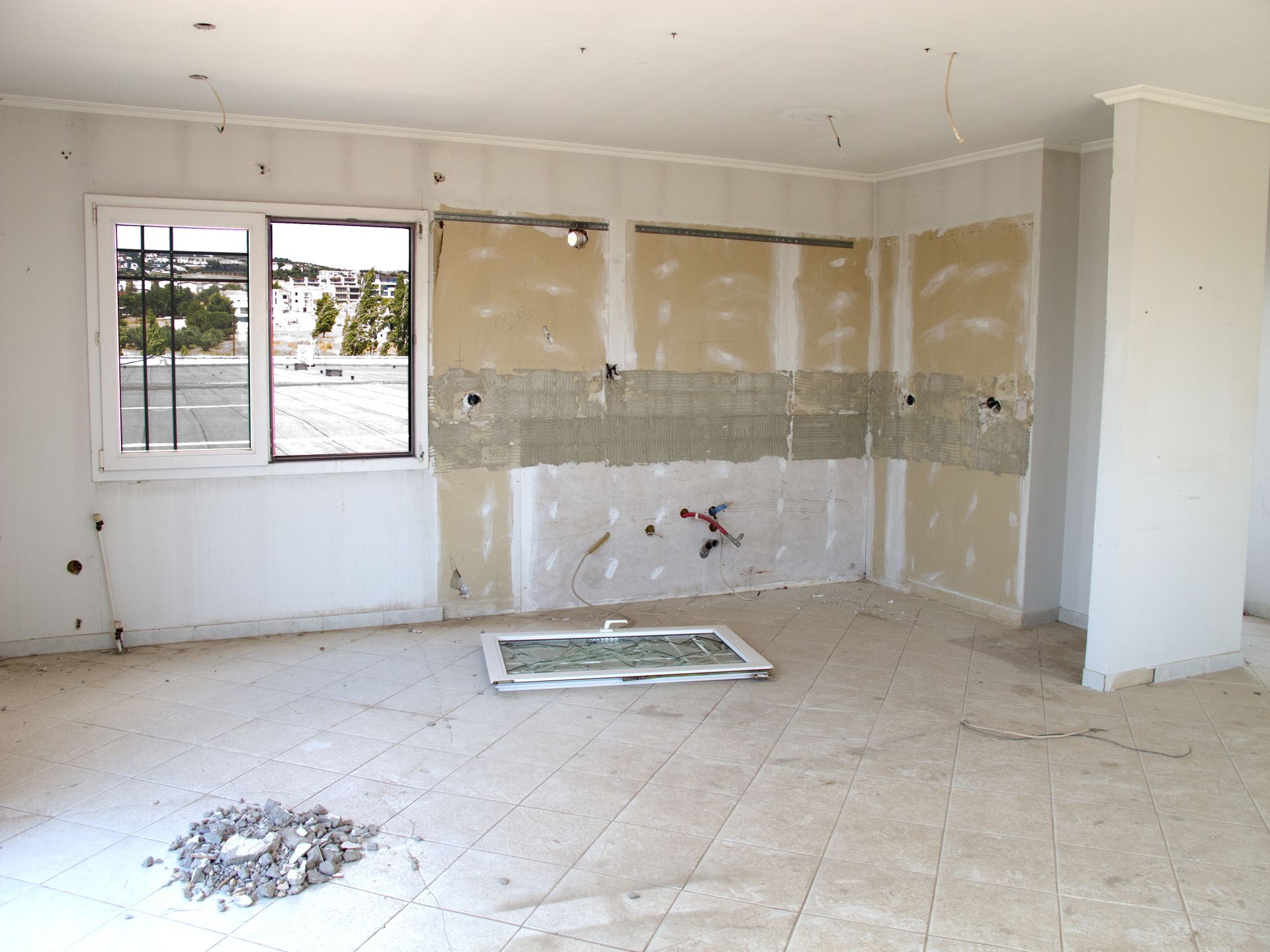 Interior of a room under construction: drywall partially installed, window, exposed wiring, debris on floor.