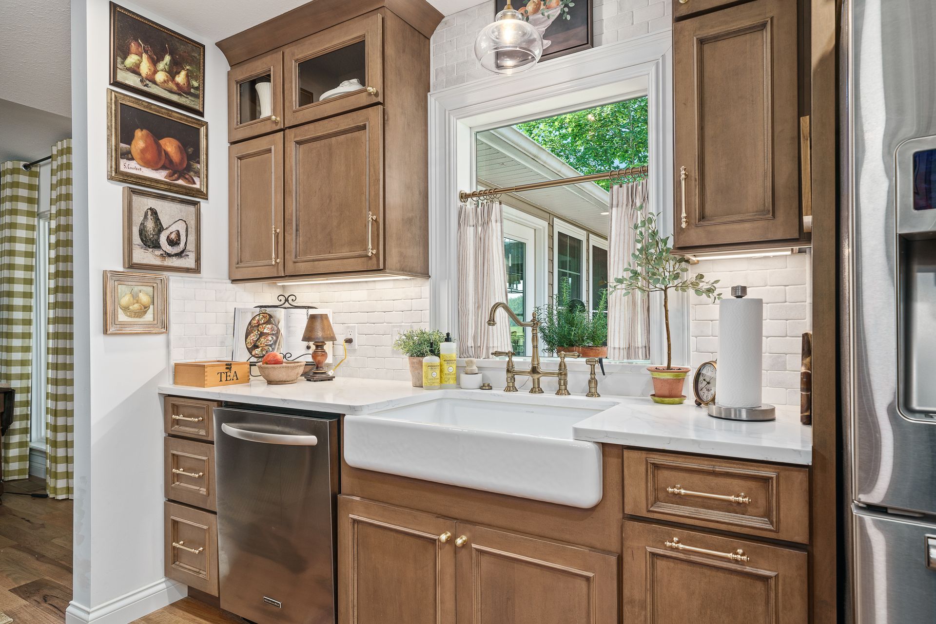 Kitchen corner with wooden cabinets, white farmhouse sink, stainless dishwasher, and fruit art on the wall.