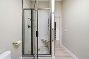 A walk-in shower with dark frames, a pebble floor, a built-in bench, and a grab bar in a neutral-toned bathroom.