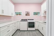 Laundry room with white cabinets, light pink walls, and matching white washer and dryer units on a grey floor.