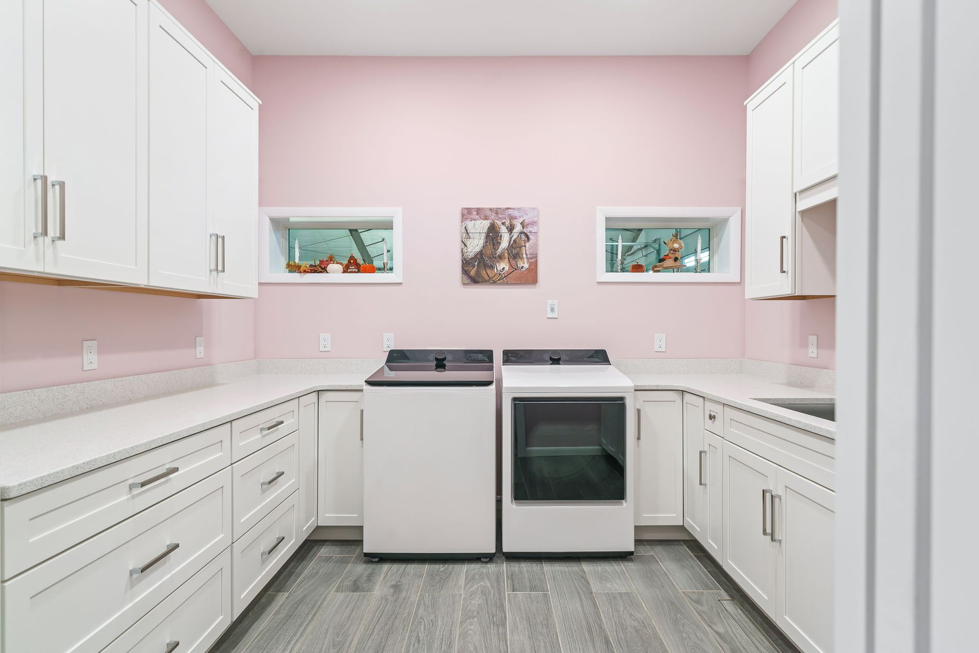 Laundry room with white cabinets, light pink walls, and matching white washer and dryer units on a grey floor.