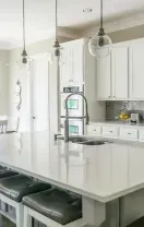 Modern kitchen with a white island, bar stools, white cabinetry, a gray tiled backsplash, and an adjacent dining area.