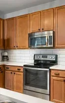 A kitchen with light wood cabinets, stainless steel appliances, white subway tile backsplash, and a white countertop.