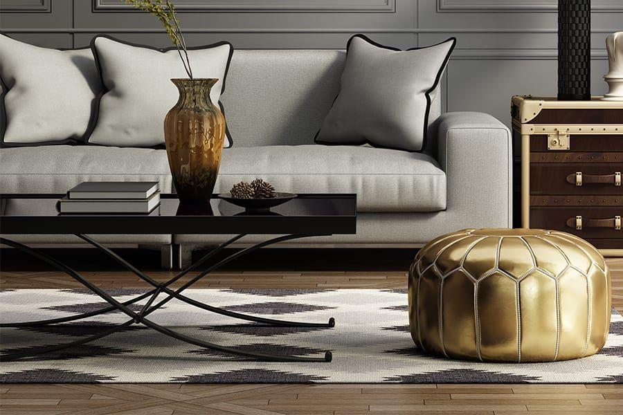A modern living room with a grey sofa, black coffee table, gold pouf, and a geometric rug on wooden floors.