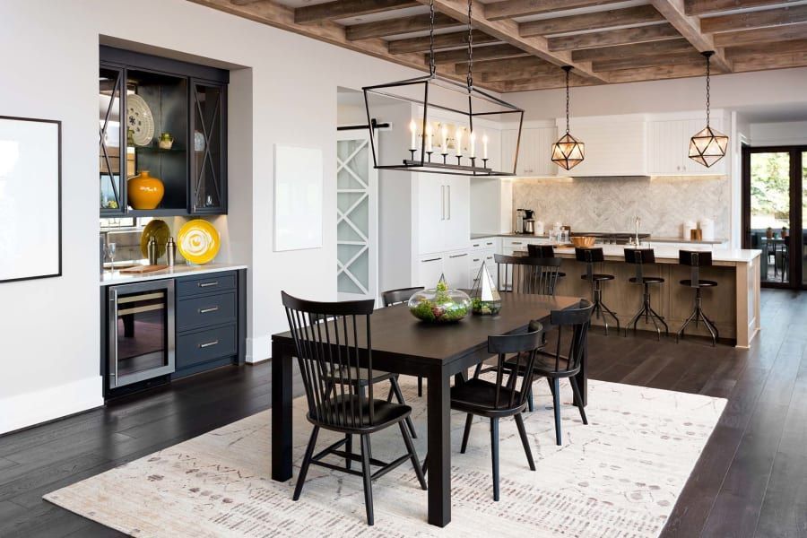 Modern dining and kitchen area with dark wood floors, a black dining table, chairs, and a bar area with yellow decor.