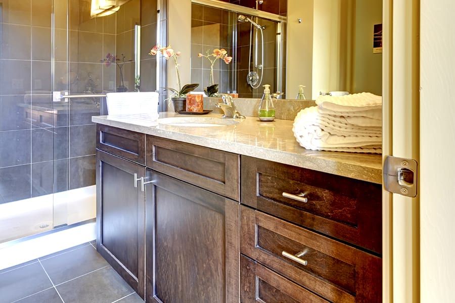 Modern bathroom with a dark wood vanity, stone countertop, stack of white towels, and a walk-in glass shower.