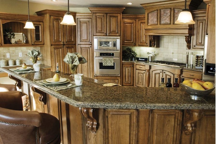A kitchen with wood cabinets, granite countertops, a built-in oven, and a breakfast bar with leather stools.