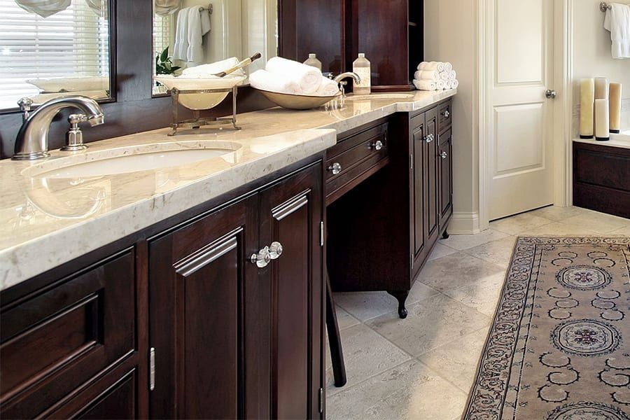 A bathroom vanity with dark wood cabinets, a light marble countertop, and decorative silver hardware.