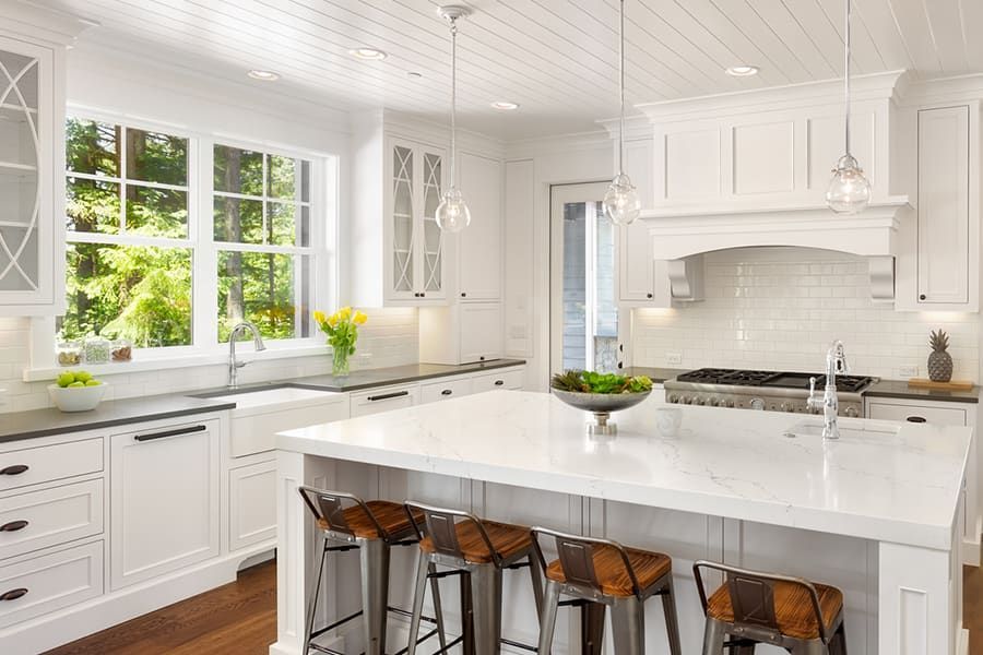 A bright, modern white kitchen featuring a large central island with bar stools, quartz countertops, and wooden floors.