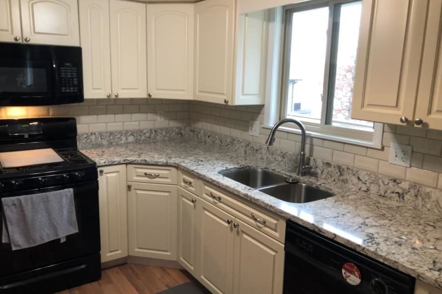 A kitchen with cream cabinets, speckled granite countertops, subway tile backsplash, and black appliances.