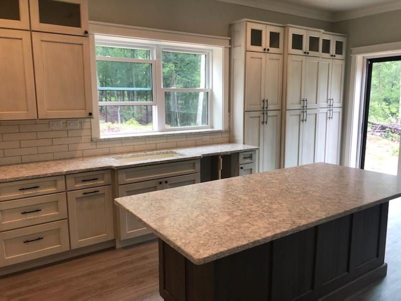 Modern kitchen featuring white cabinets, a large island with a dark base, light countertops, and a window with garden views.
