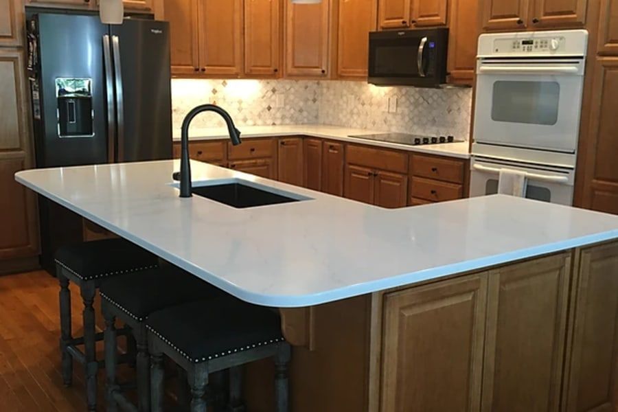 Kitchen featuring wooden cabinets, a white countertop island with a sink and bar stools, and stainless steel appliances.