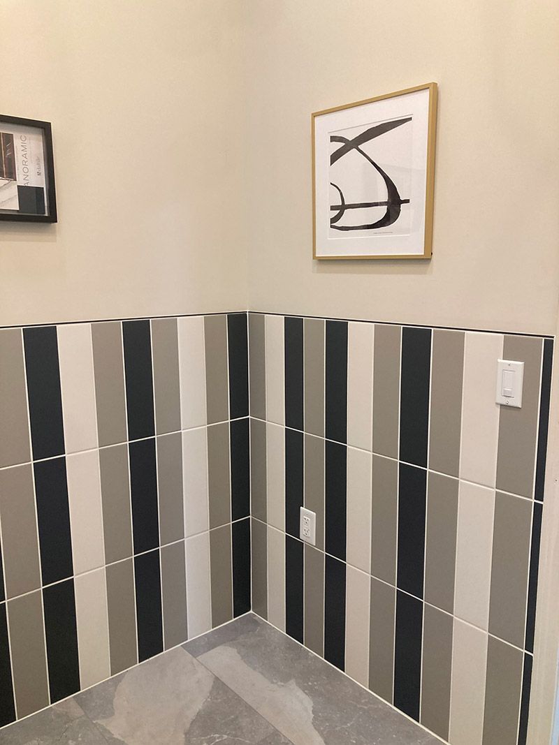 Interior corner with vertical striped wall tiles in black, grey, and cream, featuring framed art and electrical outlets.