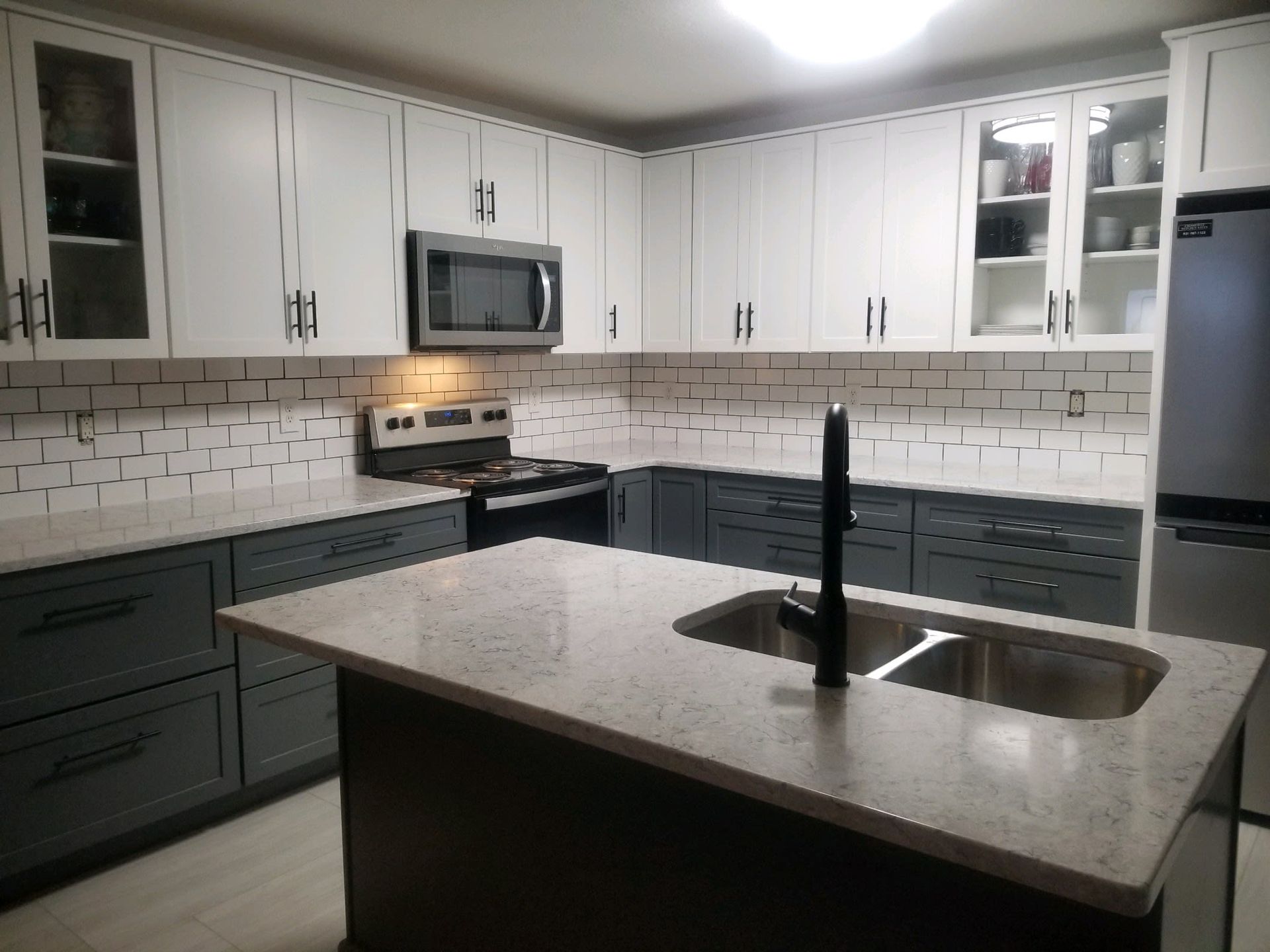 A modern kitchen features white upper cabinets, dark gray lower cabinets, light countertops, and a subway tile backsplash.