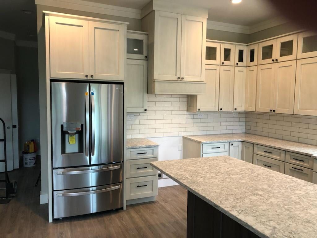 A kitchen with off-white cabinets, stainless steel refrigerator, white subway tile backsplash, and light speckled counters.