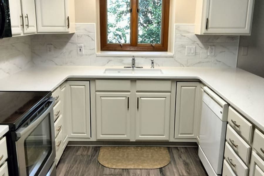 A kitchen with white cabinets, white marble-patterned backsplash, light countertops, and a stainless steel oven.