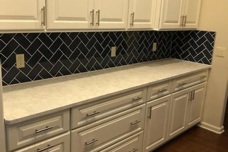 White kitchen cabinets and drawers paired with a white marble-look countertop and a black herringbone-patterned backsplash.