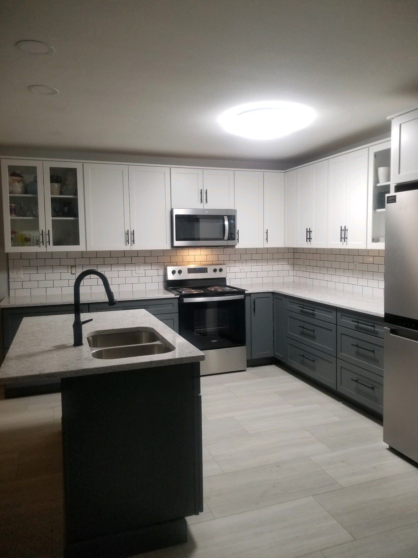 A modern kitchen with white upper cabinets, dark grey lower cabinets, a central island, and a stainless steel stove.