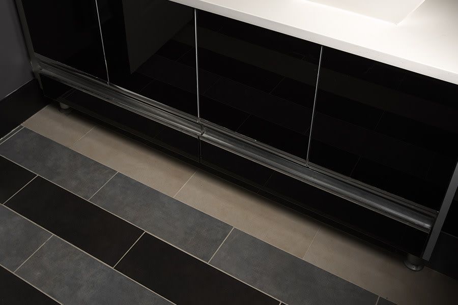 A high-angle view of a sleek black bathroom vanity cabinet above a floor featuring alternating black and gray tile strips.
