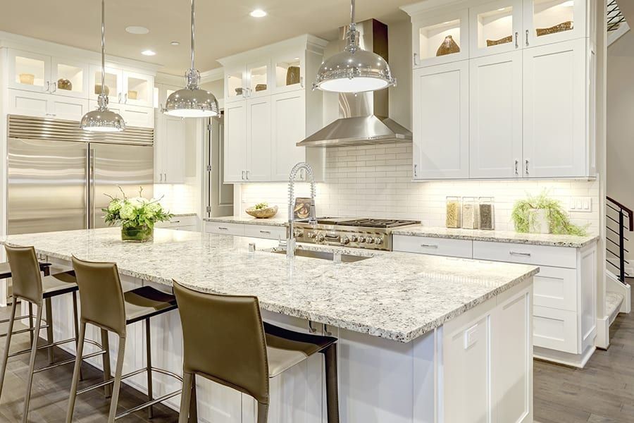 A bright, modern kitchen featuring white cabinets, a large granite island, stainless steel appliances, and pendant lights.