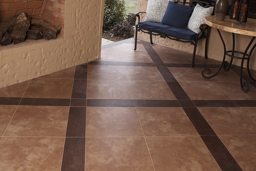 A patio features large brown square tiles accented by dark brown rectangular tiles arranged in a grid pattern.
