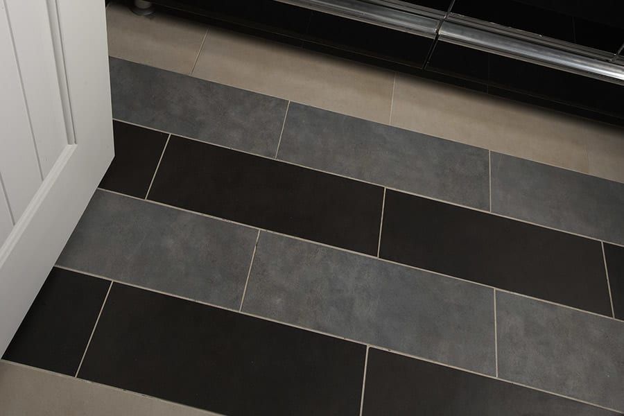 A floor with a patterned design of alternating dark gray and black rectangular tiles next to a white door frame.
