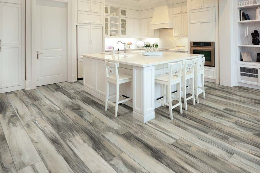 Modern white kitchen with a center island, bar stools, and light-colored wood-grain tile flooring.