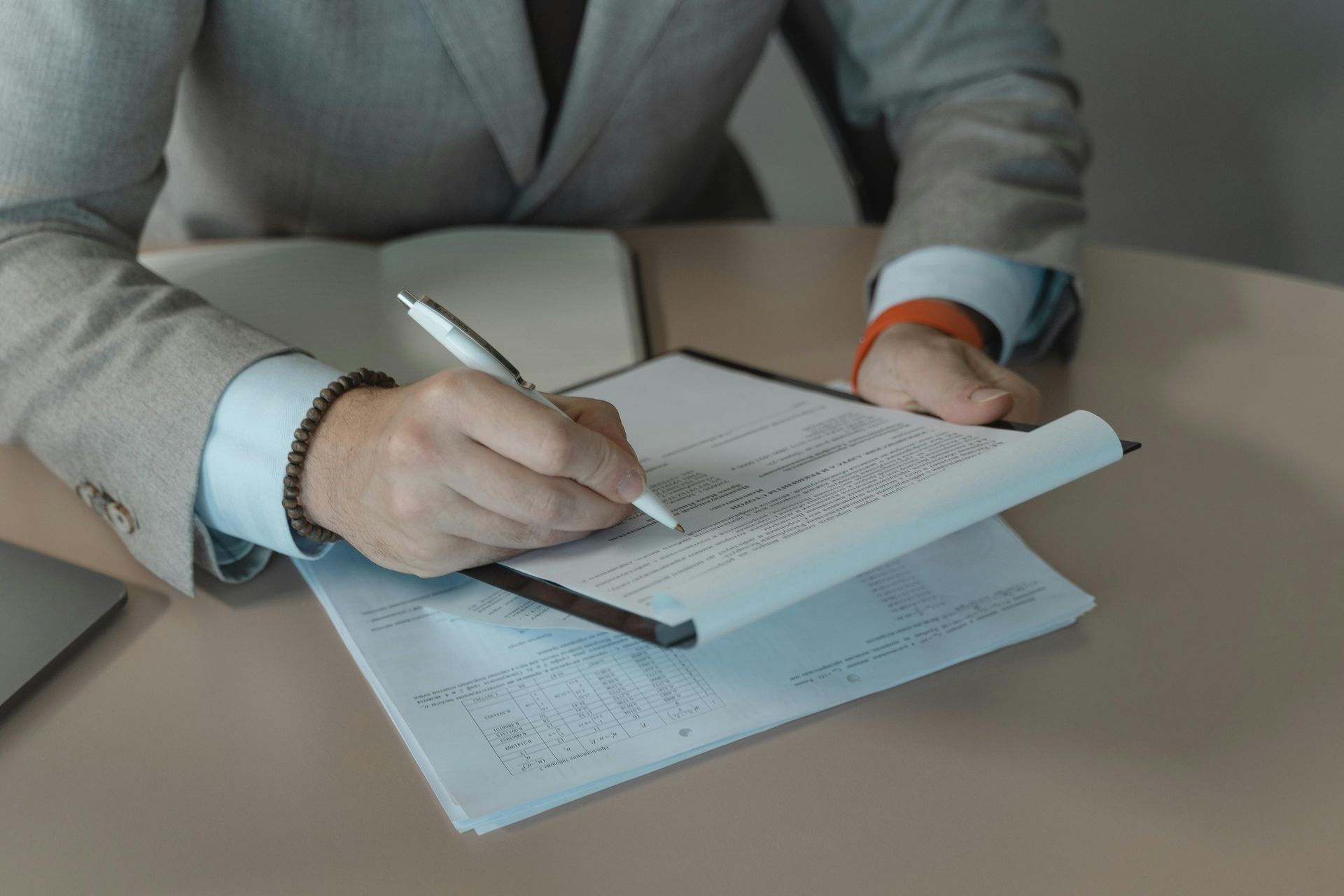 Person in a suit writing on paperwork at a desk.