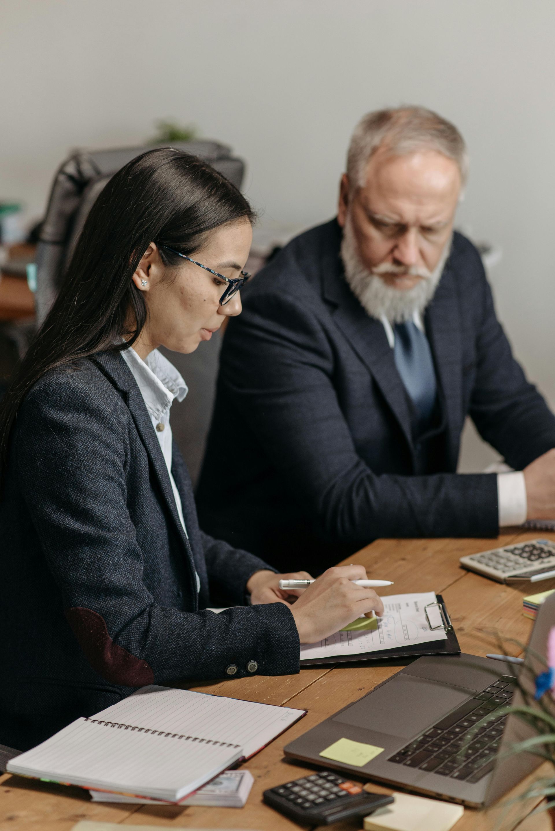 Woman and older man reviewing documents at a wooden table. The woman is writing, and the man is looking down.