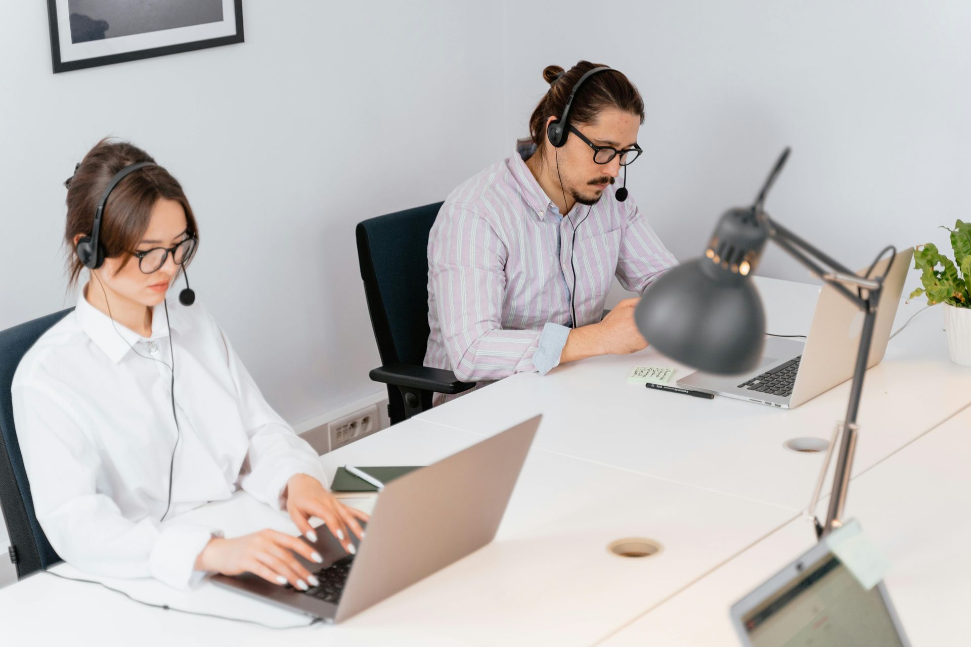 Two people with headsets working on laptops at desks in an office.