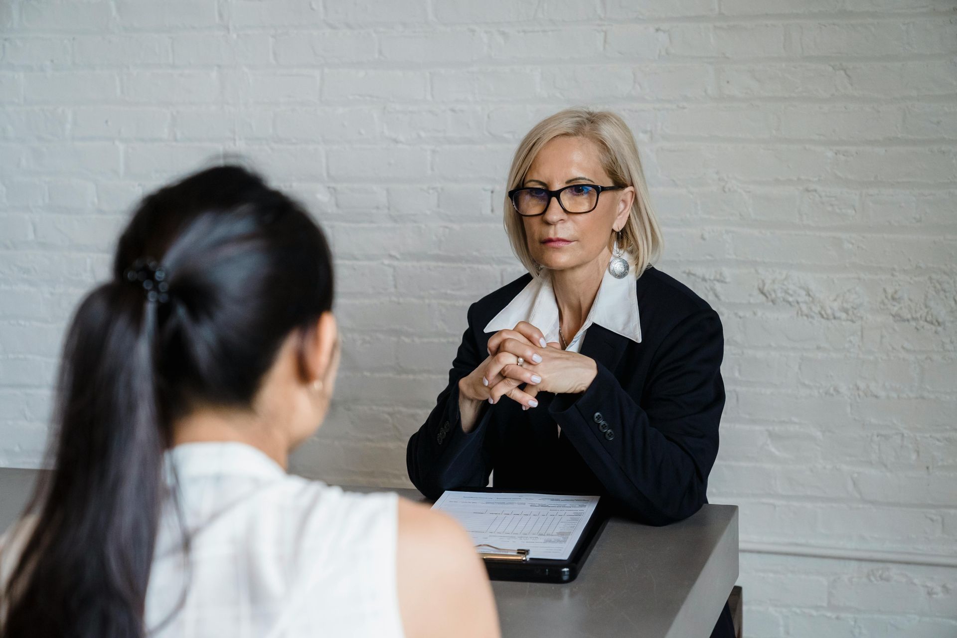 Woman interviewing another woman at a table; they're in an office setting.