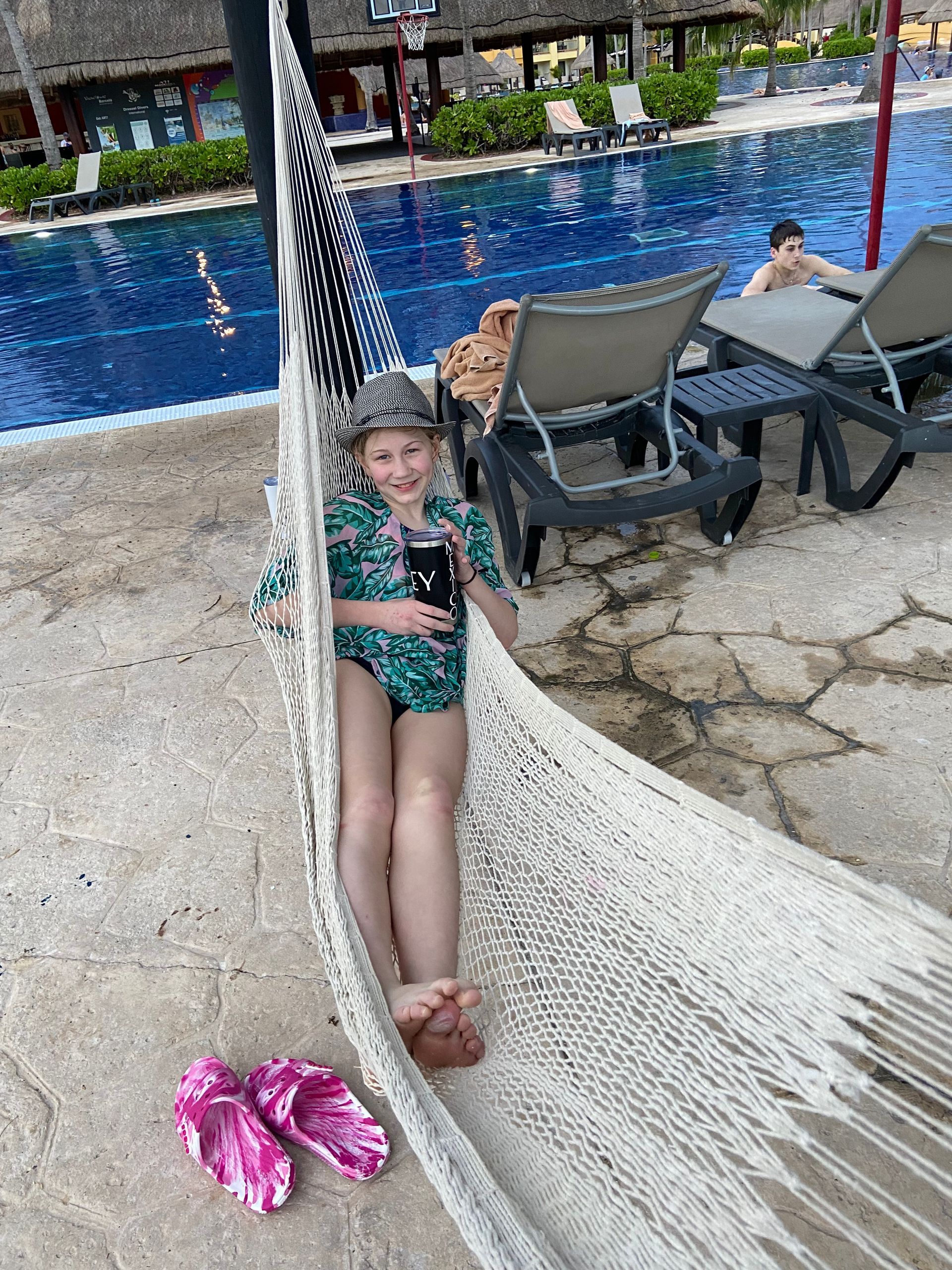 A little girl is sitting in a hammock next to a pool.