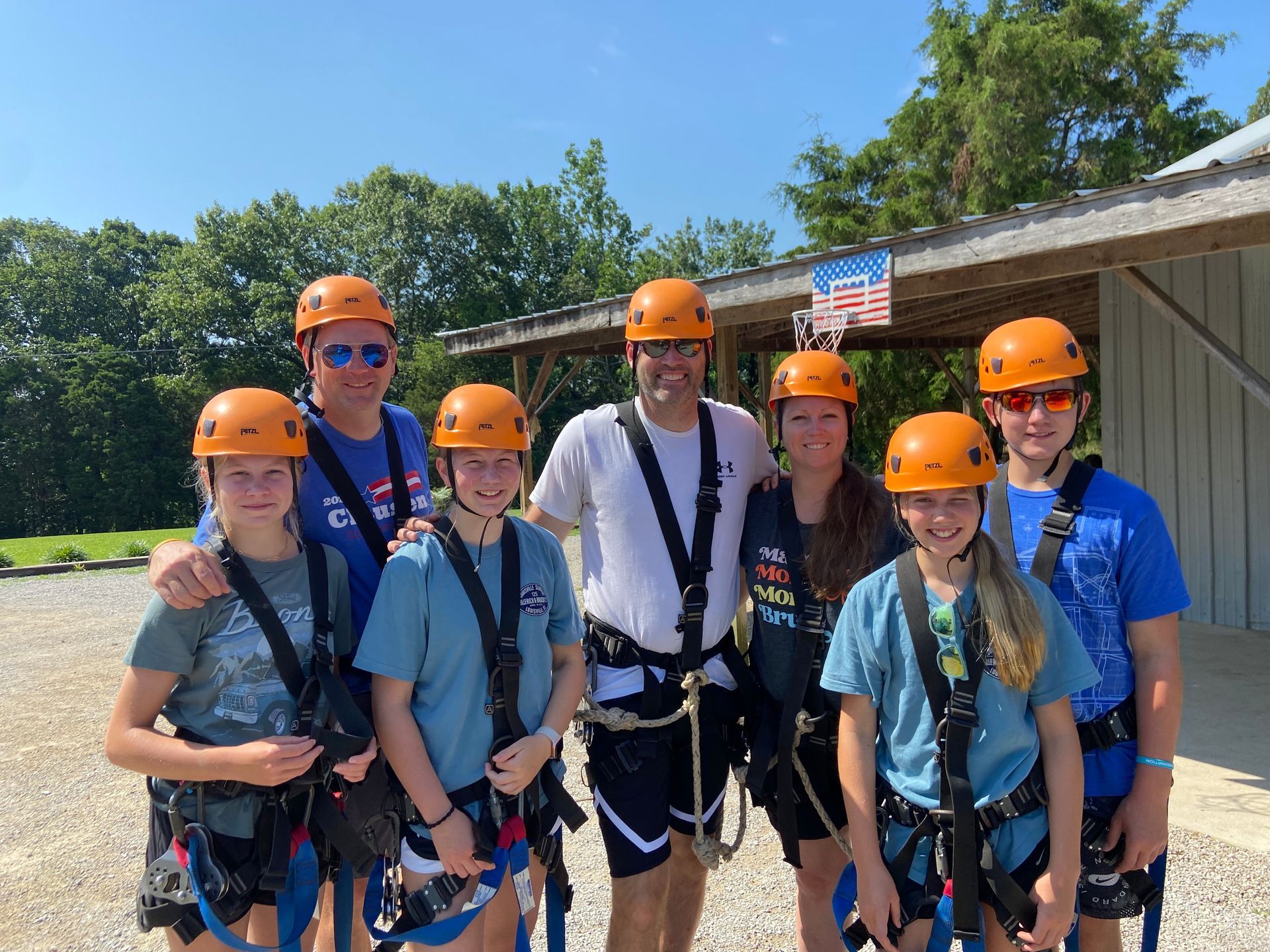 A group of people wearing helmets and harnesses are posing for a picture ready to go ziplining.
