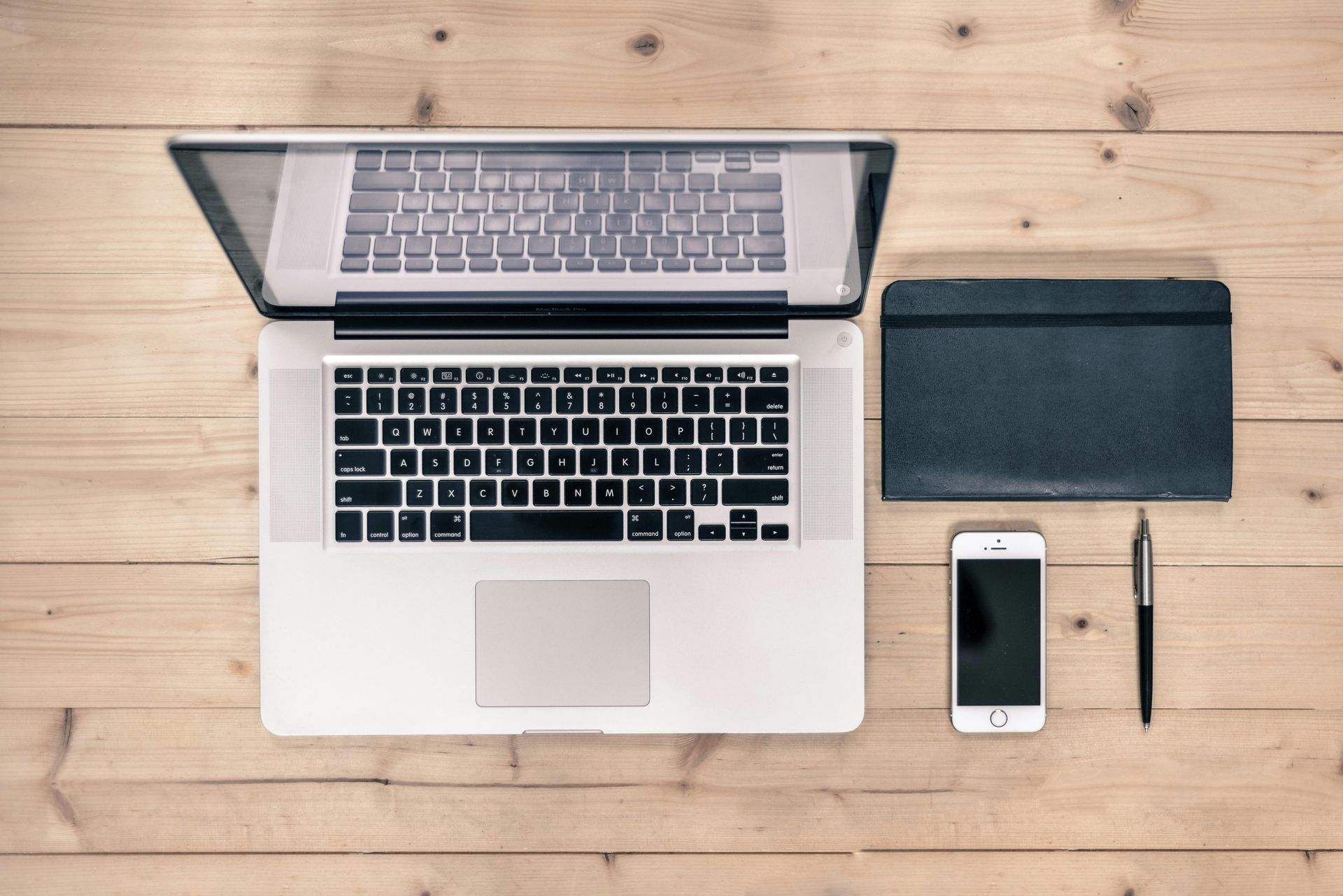 A laptop computer is sitting on a wooden table next to a cell phone and a pen.