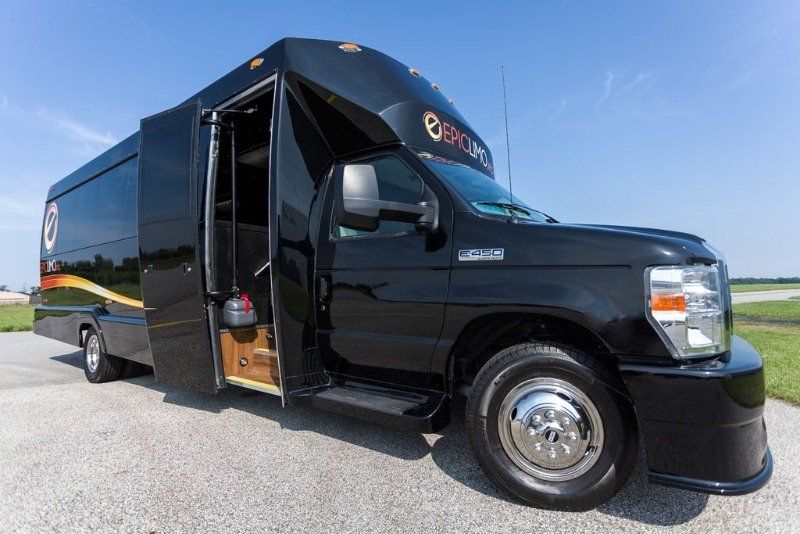 Black party bus with open door, parked on a paved surface outdoors.