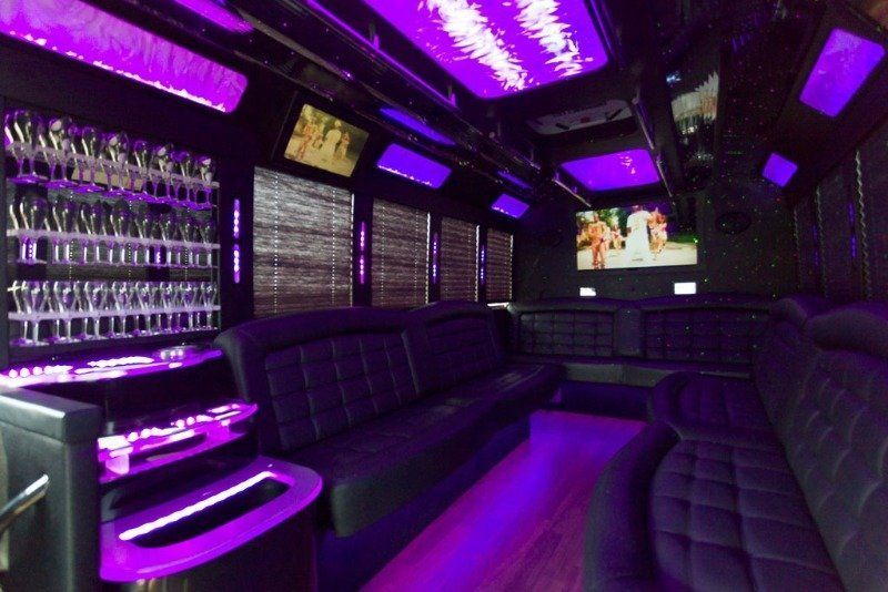 Inside a party bus with purple lights, leather seats, and a wall of champagne glasses.